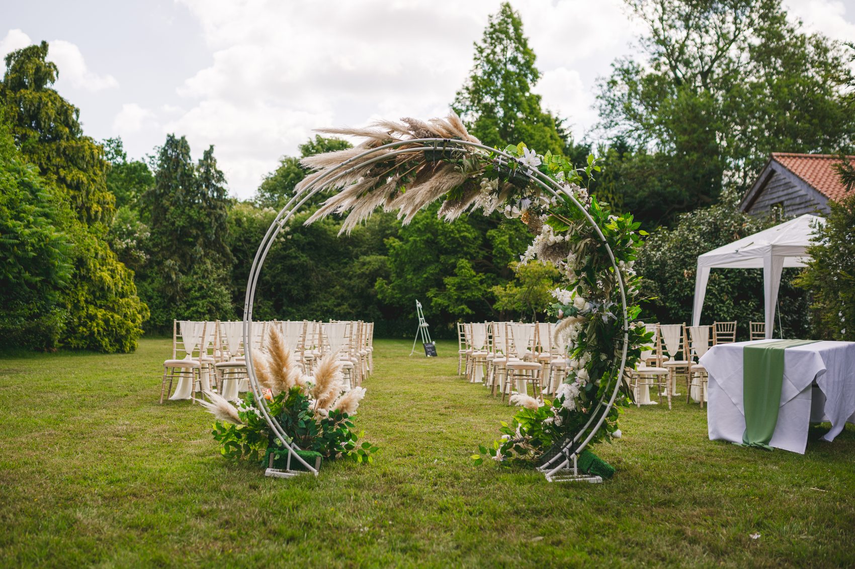 An outdoor ceremony with a pampas moon arch on the lawns at Ivy House
