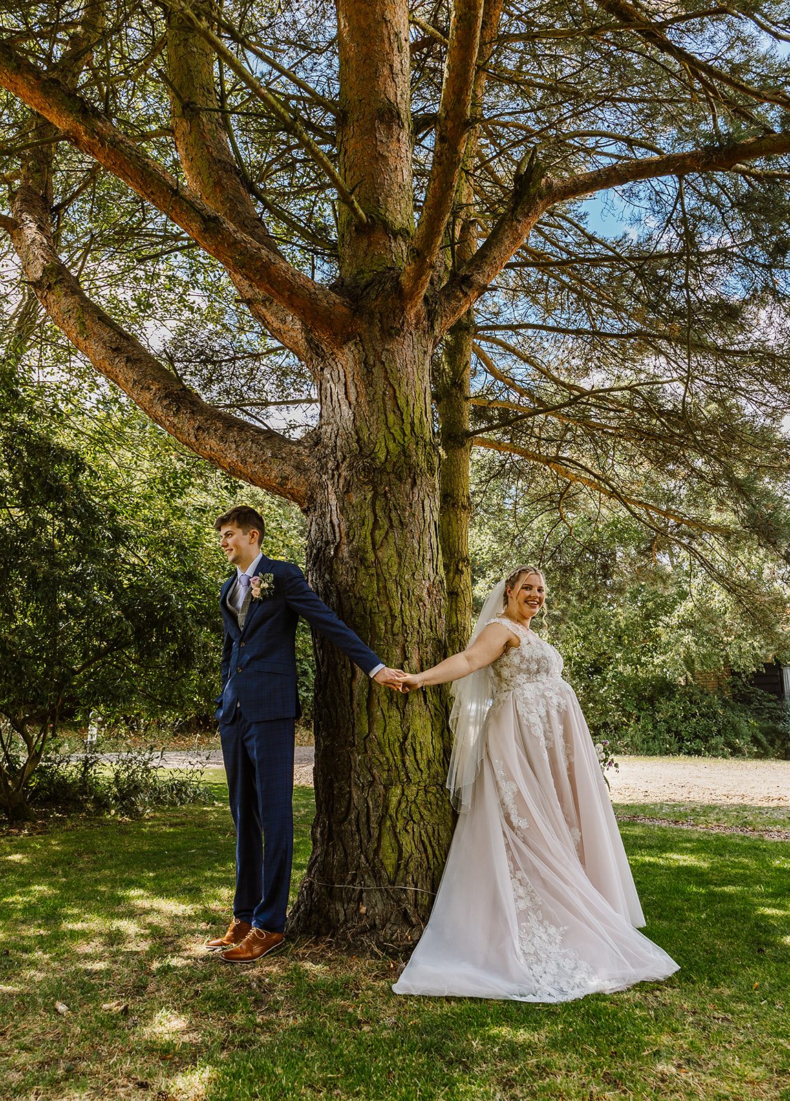 Newlyweds beneath a grand tree in the gardens at Ivy House
